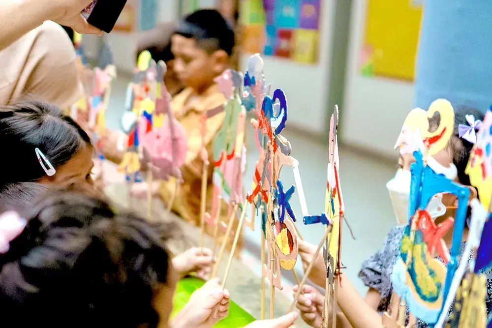 A group of children are playing with paper puppets in a classroom.