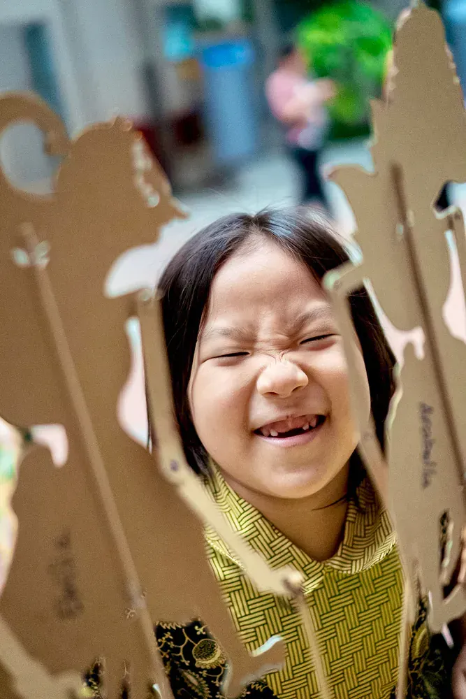 A young girl is making a funny face while holding a cardboard puppet.