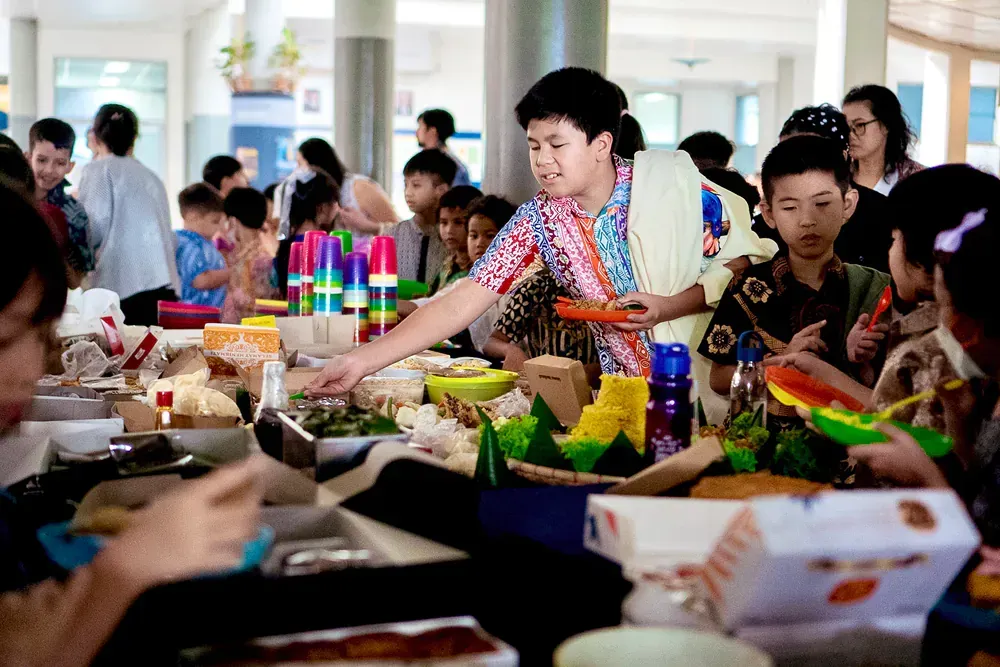 A man is serving food to a group of children at a table.