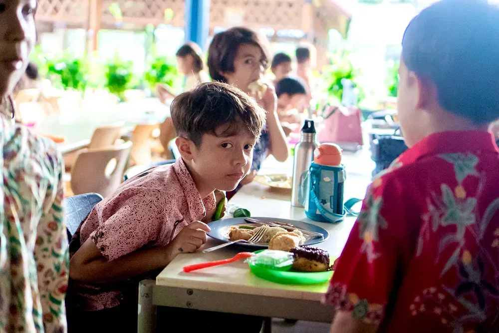 A group of children are sitting at a table eating food.