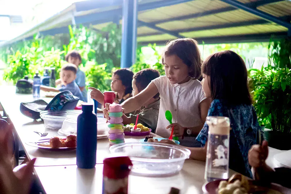 A group of children are sitting at a long table eating food.