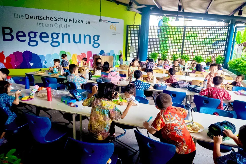 A group of children are sitting at tables in a cafeteria.