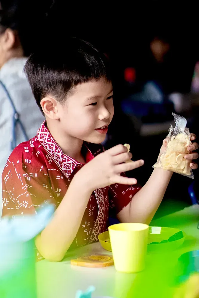 A young boy is sitting at a table holding a bag of food.