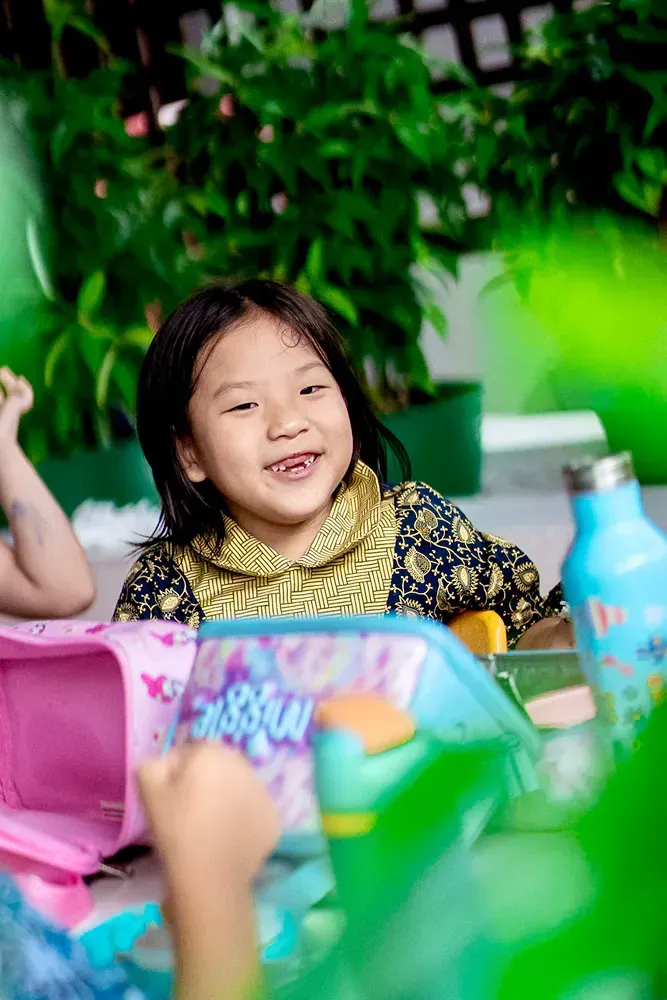 A little girl is sitting at a table with a lunch box and a water bottle.