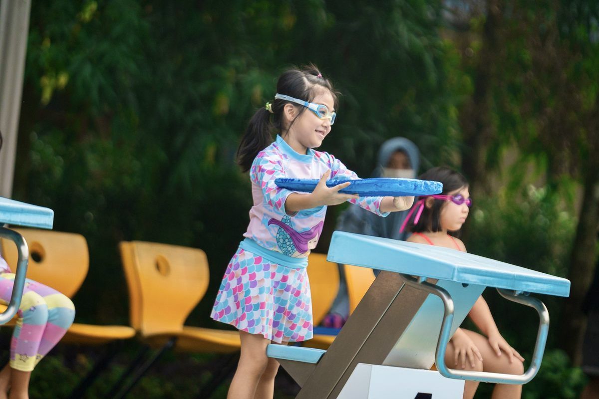 A little girl is standing on a starting block in a swimming pool.