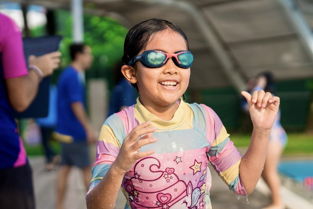 A little girl wearing sunglasses and a swimsuit is standing in the water.