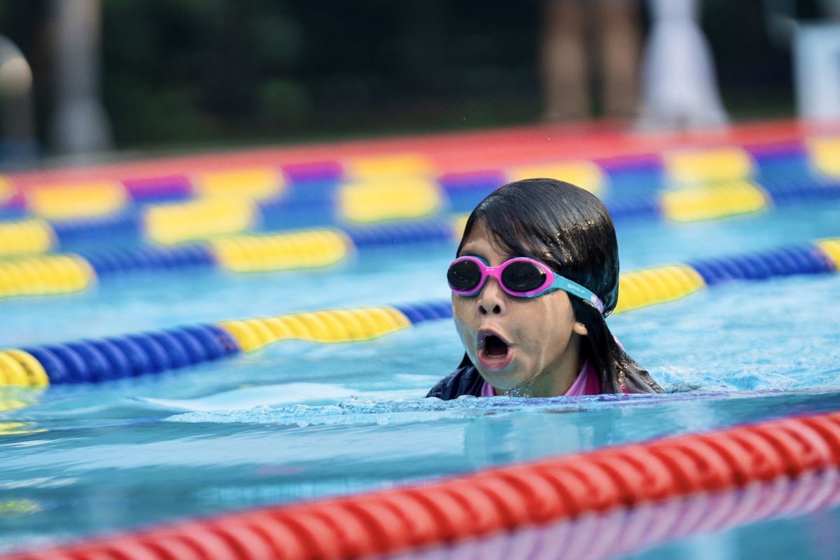 A young girl wearing goggles is swimming in a swimming pool.