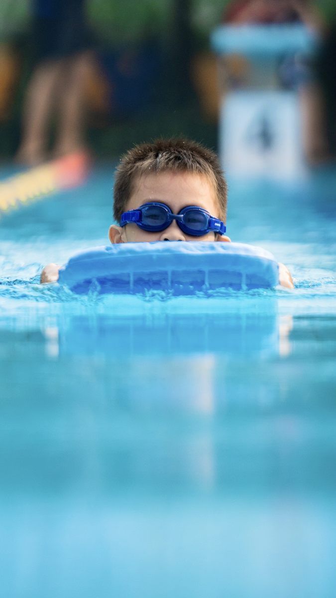 A young boy wearing goggles is swimming in a pool.
