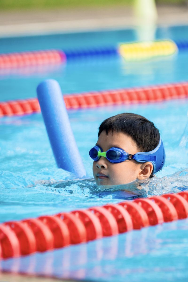 A young boy wearing goggles is swimming in a pool.