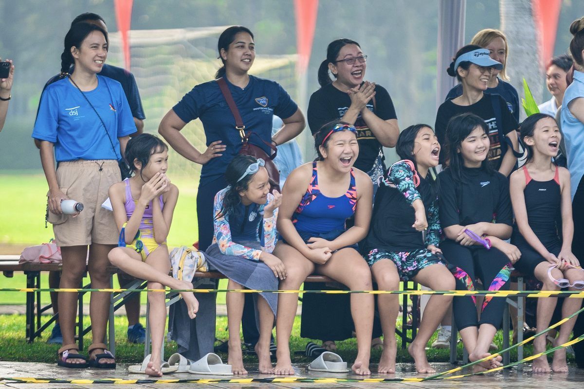 A group of young girls are sitting on a bench watching a swimming race.