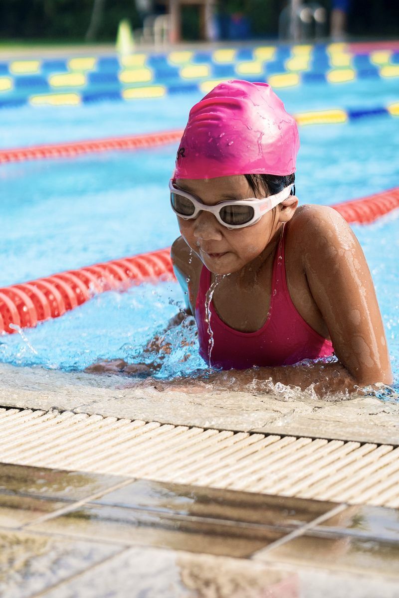 A young girl is swimming in a pool wearing a pink cap and goggles.