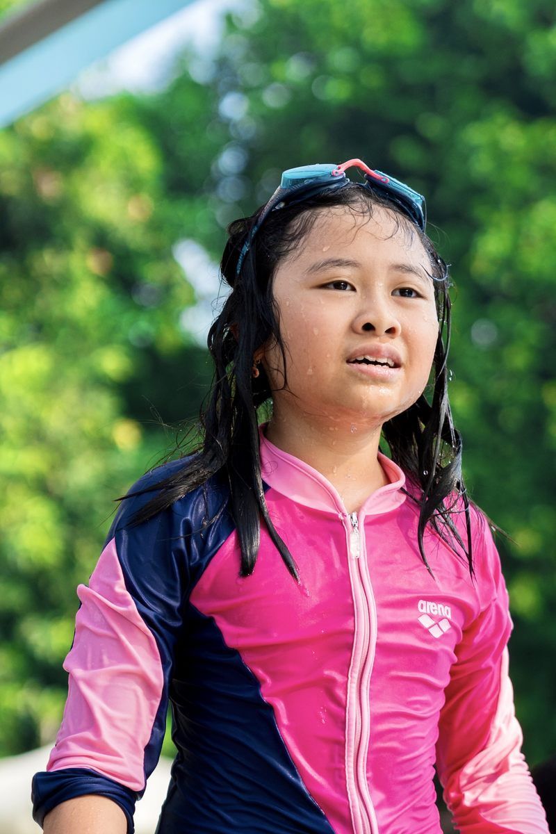 A young girl is wearing a pink and blue swimsuit and sunglasses.
