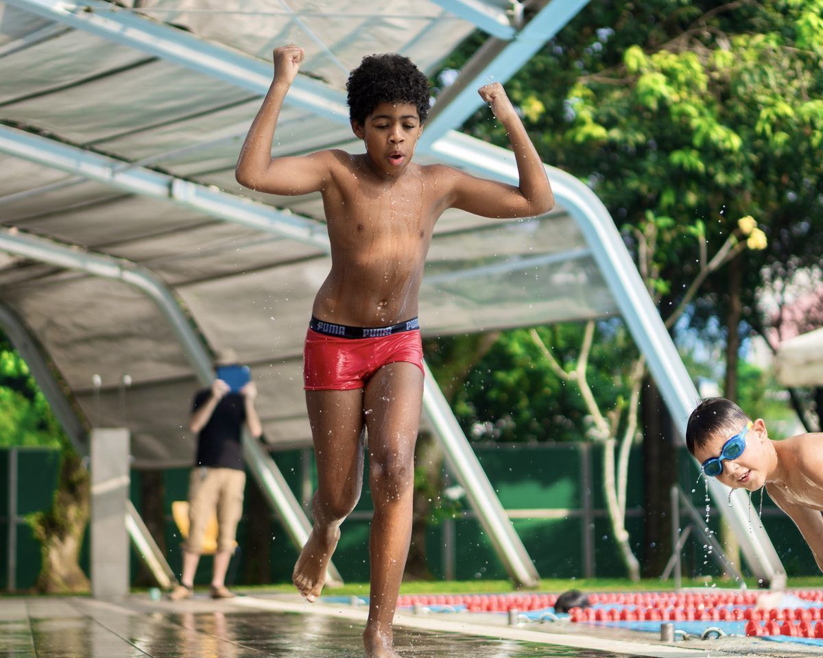 A boy in red swim trunks is mid-jump on a water obstacle course