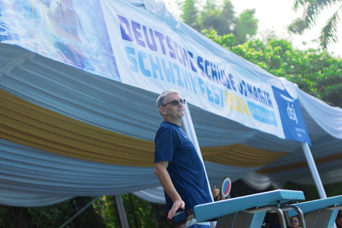 A man is standing in front of a sign that says schwimmfest
