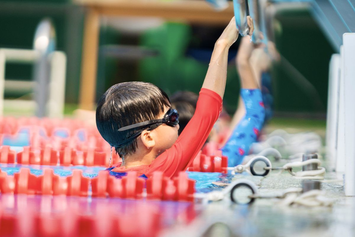 A young boy wearing goggles is getting ready to swim in a pool.