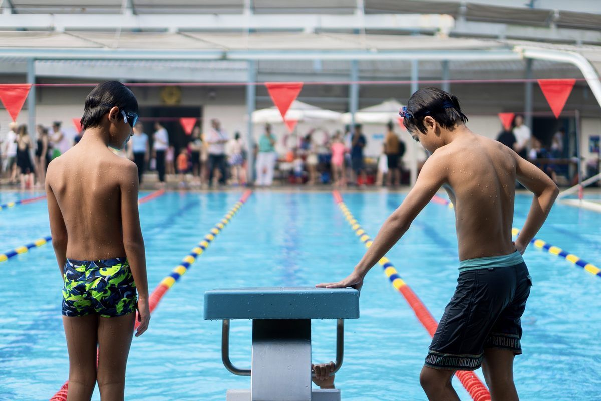 Two young boys are standing on the starting block of a swimming pool.
