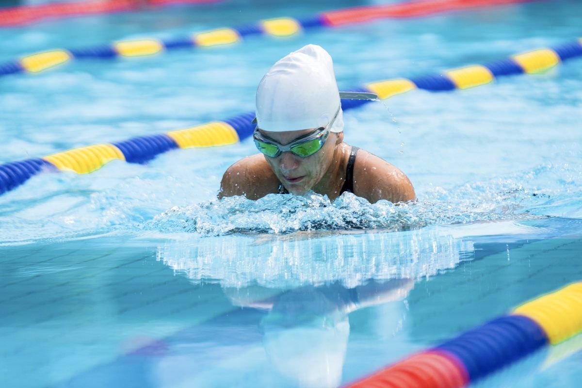 A woman is swimming in a swimming pool wearing a swim cap and goggles.