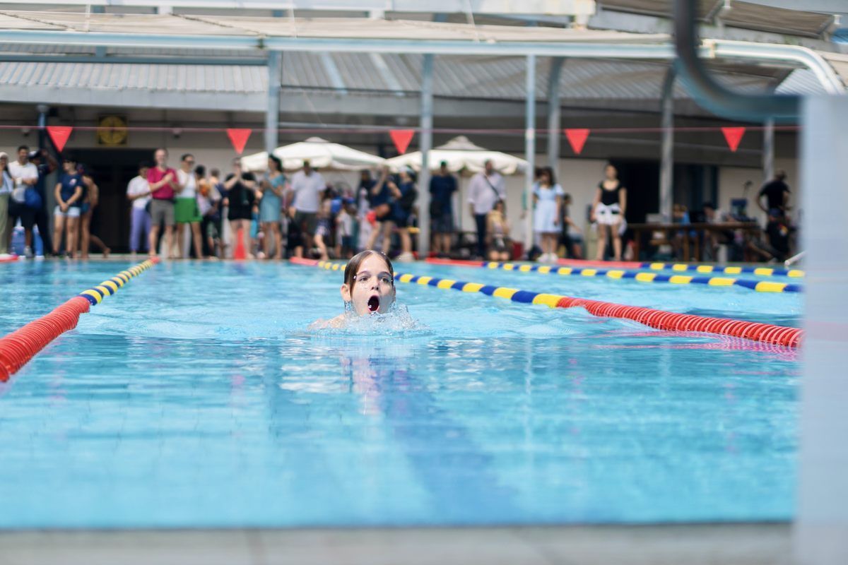 A boy is swimming in a pool with a crowd watching.