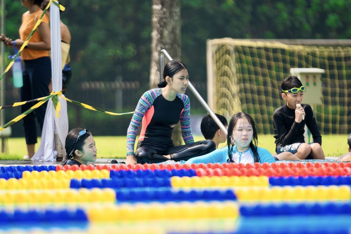 A group of people are sitting on the edge of a swimming pool.
