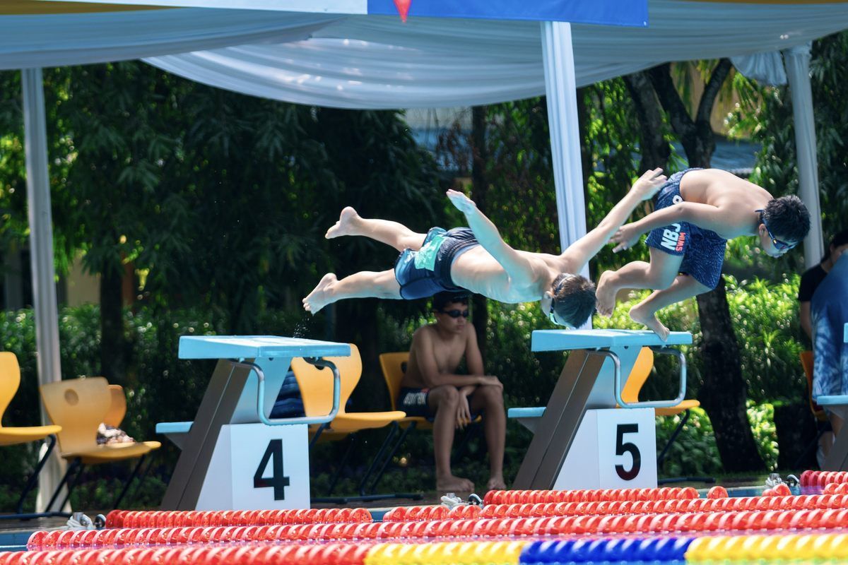 A man is diving into a pool with the number 4 and 5 in the background