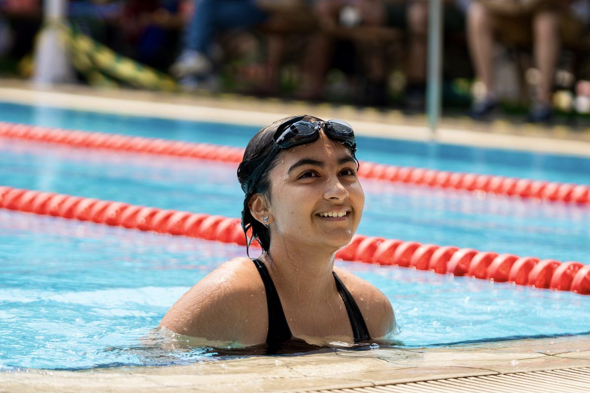 A young girl is smiling while swimming in a swimming pool.
