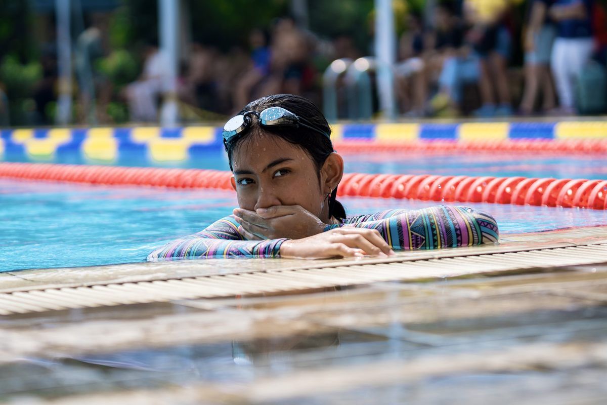 A woman is leaning on the edge of a swimming pool.