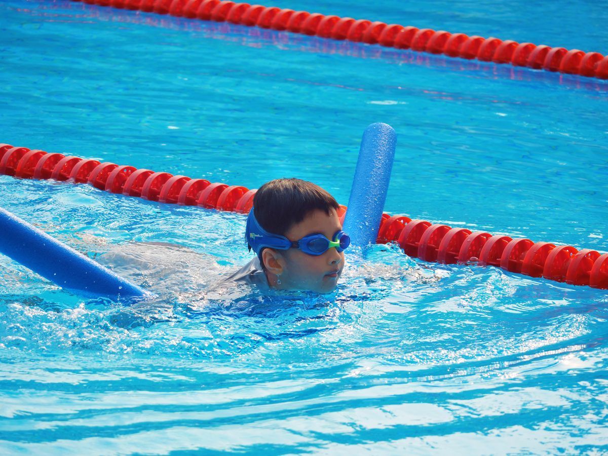 A man is swimming in a pool with foam noodles.