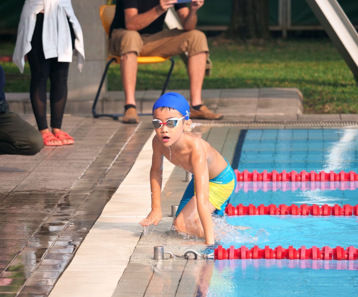 A young boy is kneeling on the edge of a swimming pool