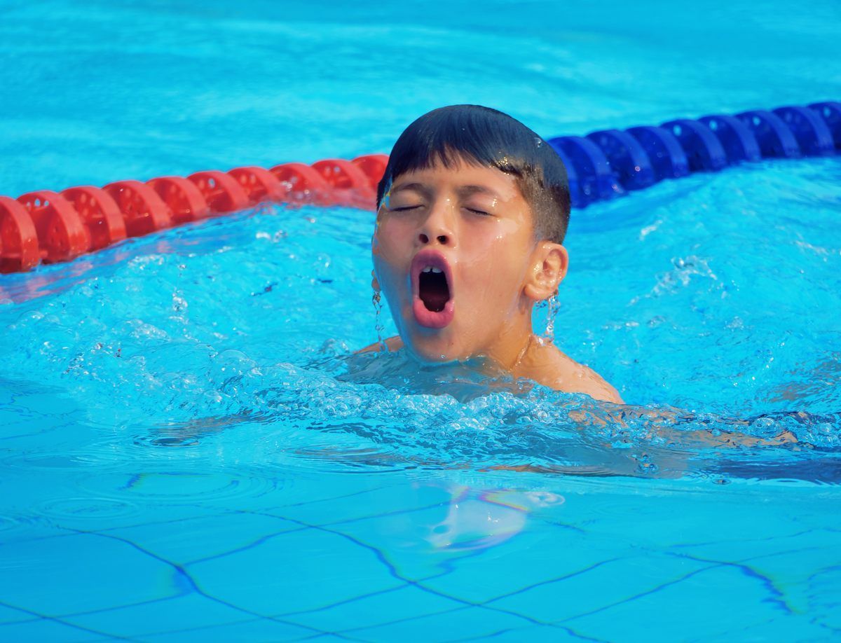A young boy is swimming in a pool with his mouth open.