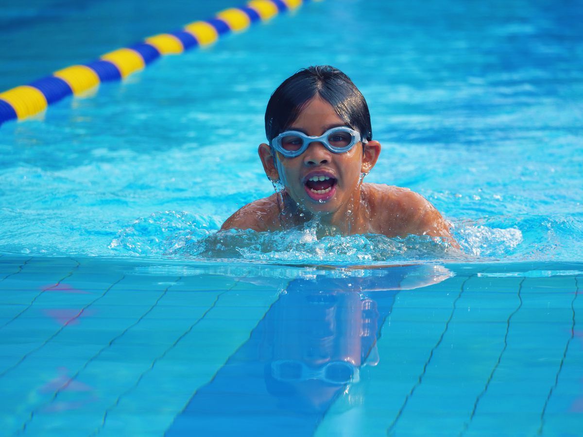 A young boy wearing goggles is swimming in a swimming pool.