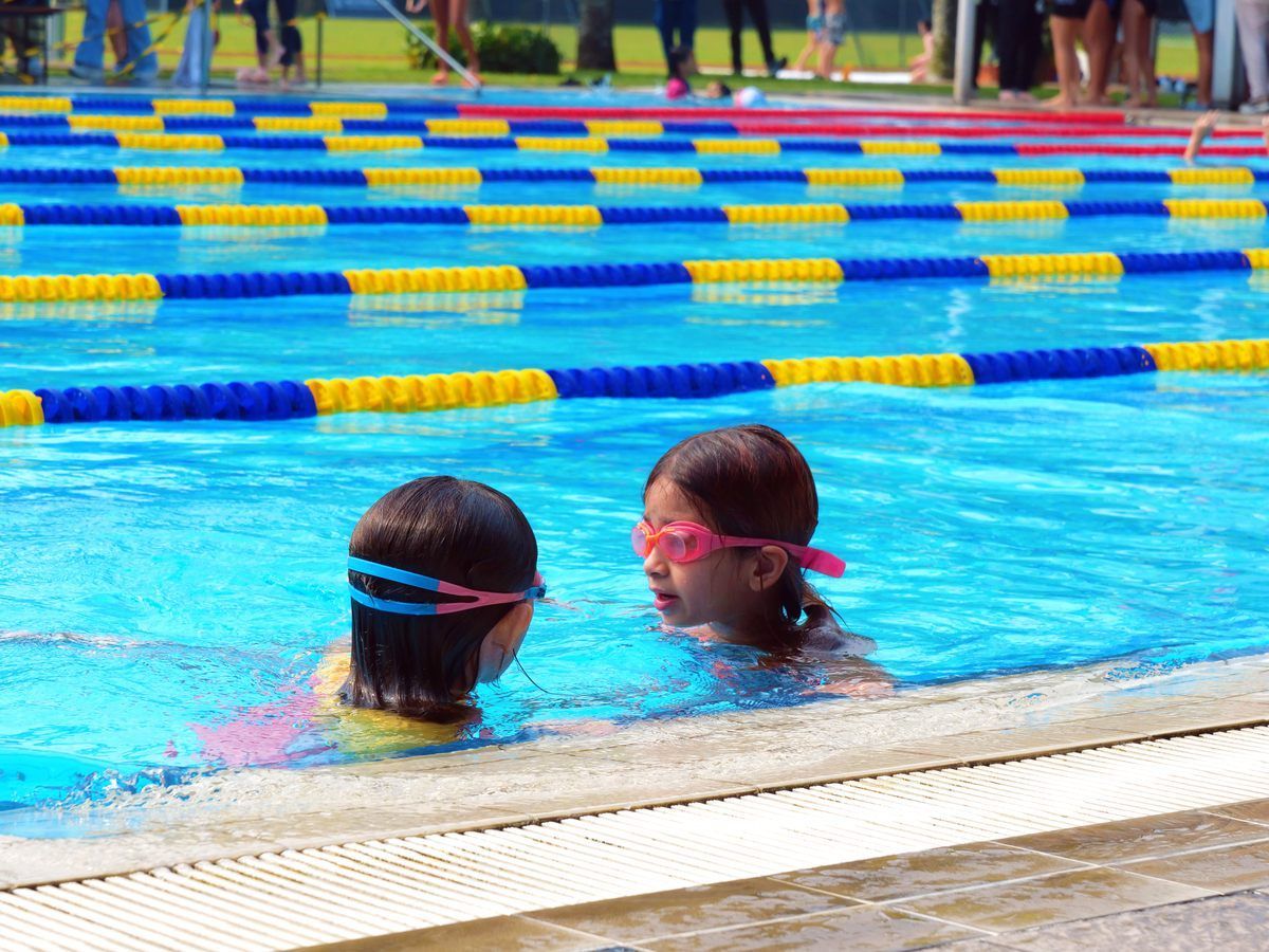 Two young girls are swimming in a swimming pool.