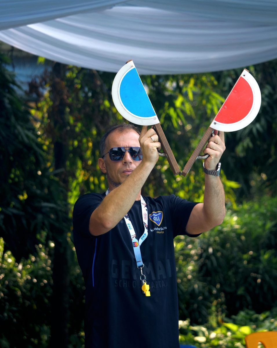 A man wearing sunglasses and a black shirt is holding a red and blue paddle