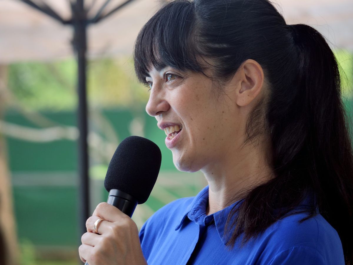 A woman in a blue shirt is holding a microphone and smiling.
