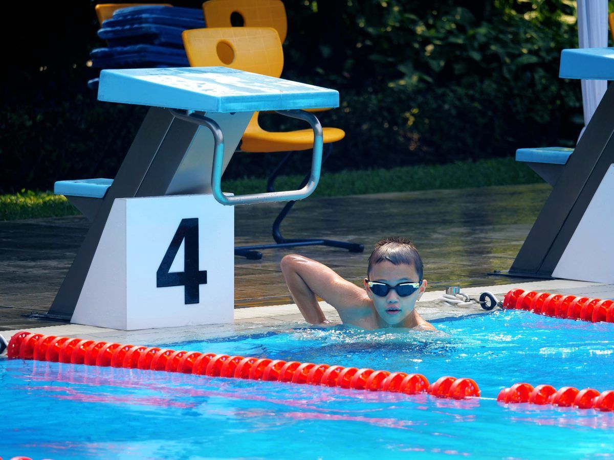 A young boy is swimming in a pool with a block with the number 4 on it