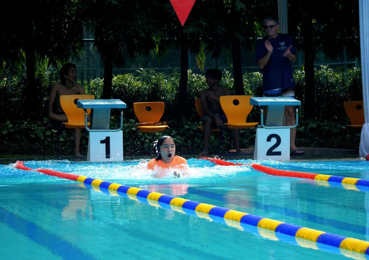 A person is swimming in a pool with blocks 1 and 2 in the background