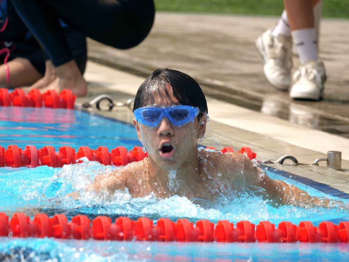 A young boy wearing goggles is swimming in a pool.