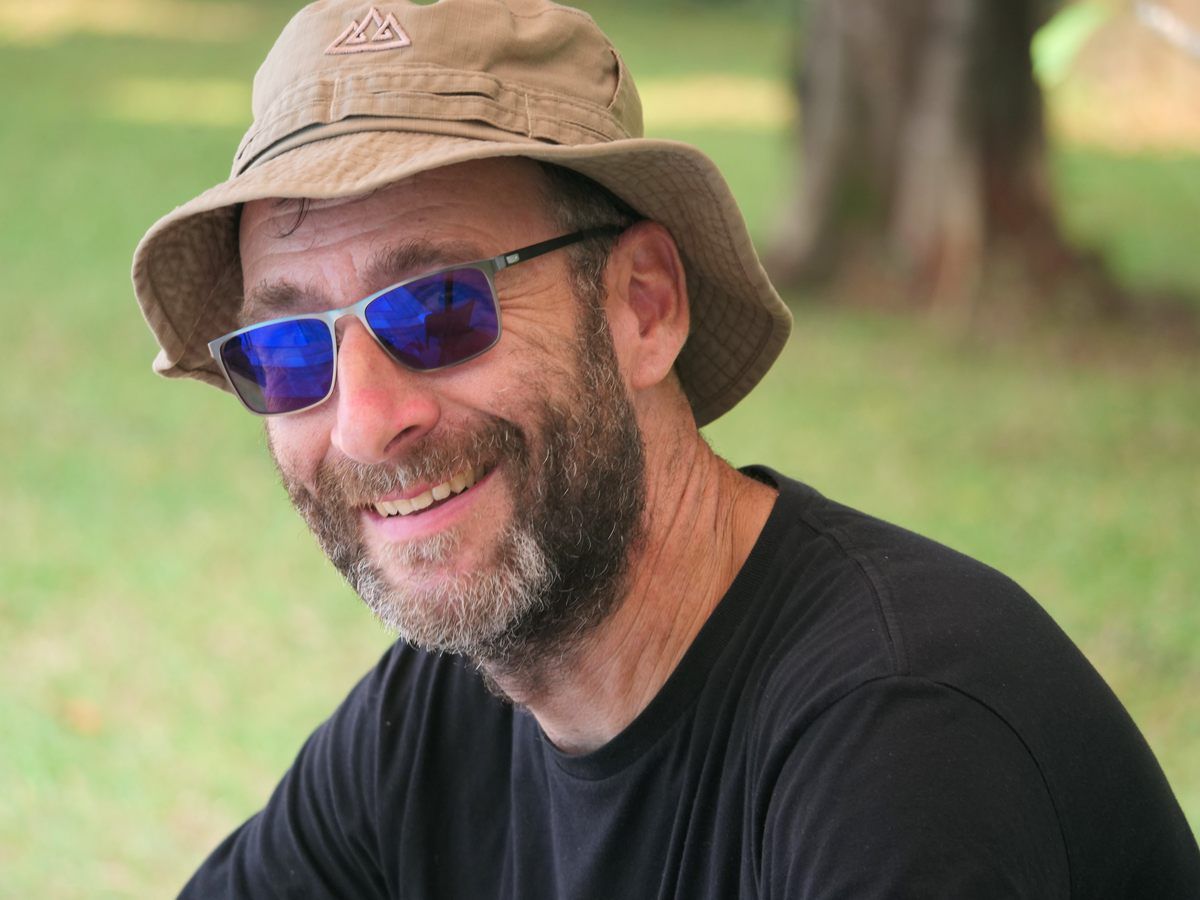 A man wearing a hat and sunglasses is smiling