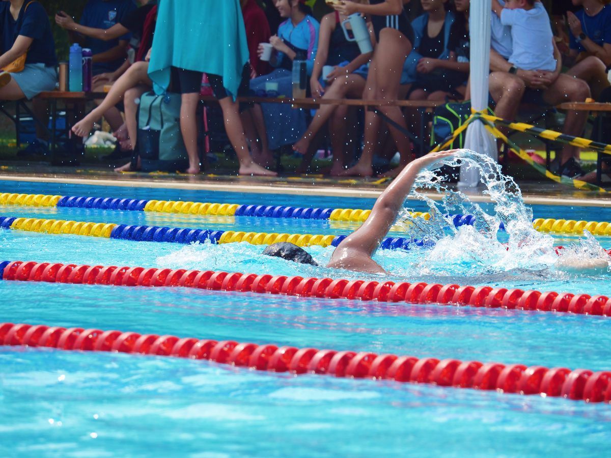 A man is swimming in a pool with a crowd watching