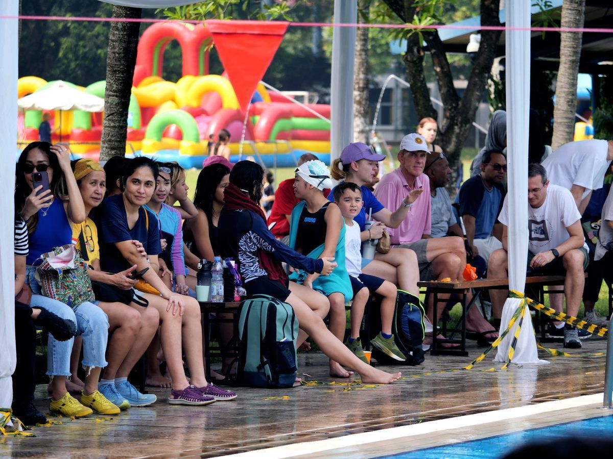 A group of people are sitting on a bench near a swimming pool.