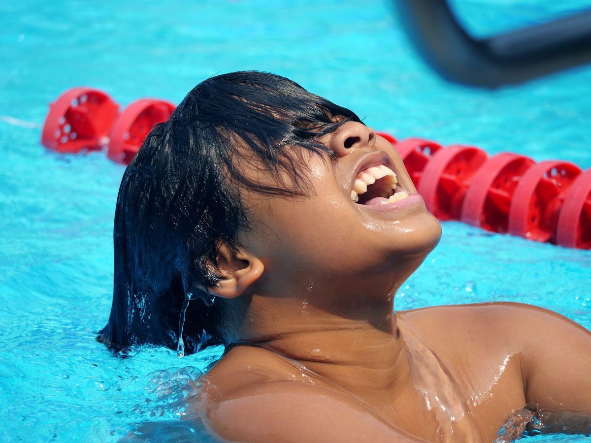 A young swimmer emerges from the pool, smiling with joy and excitement near a red lane marker.