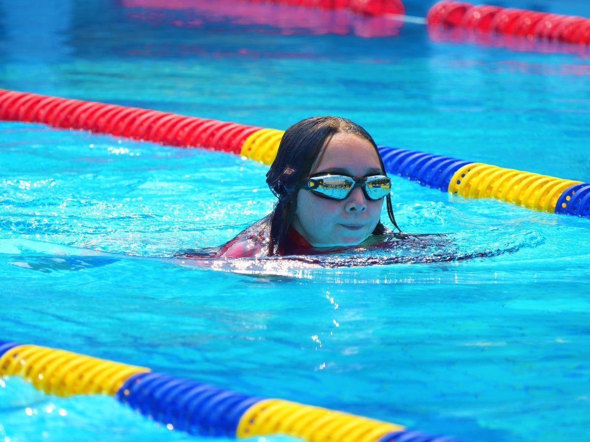 A young girl wearing goggles is swimming in a pool