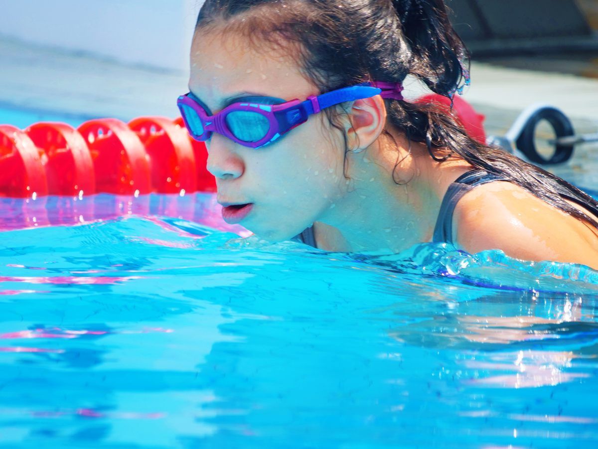 A woman wearing goggles is swimming in a pool.
