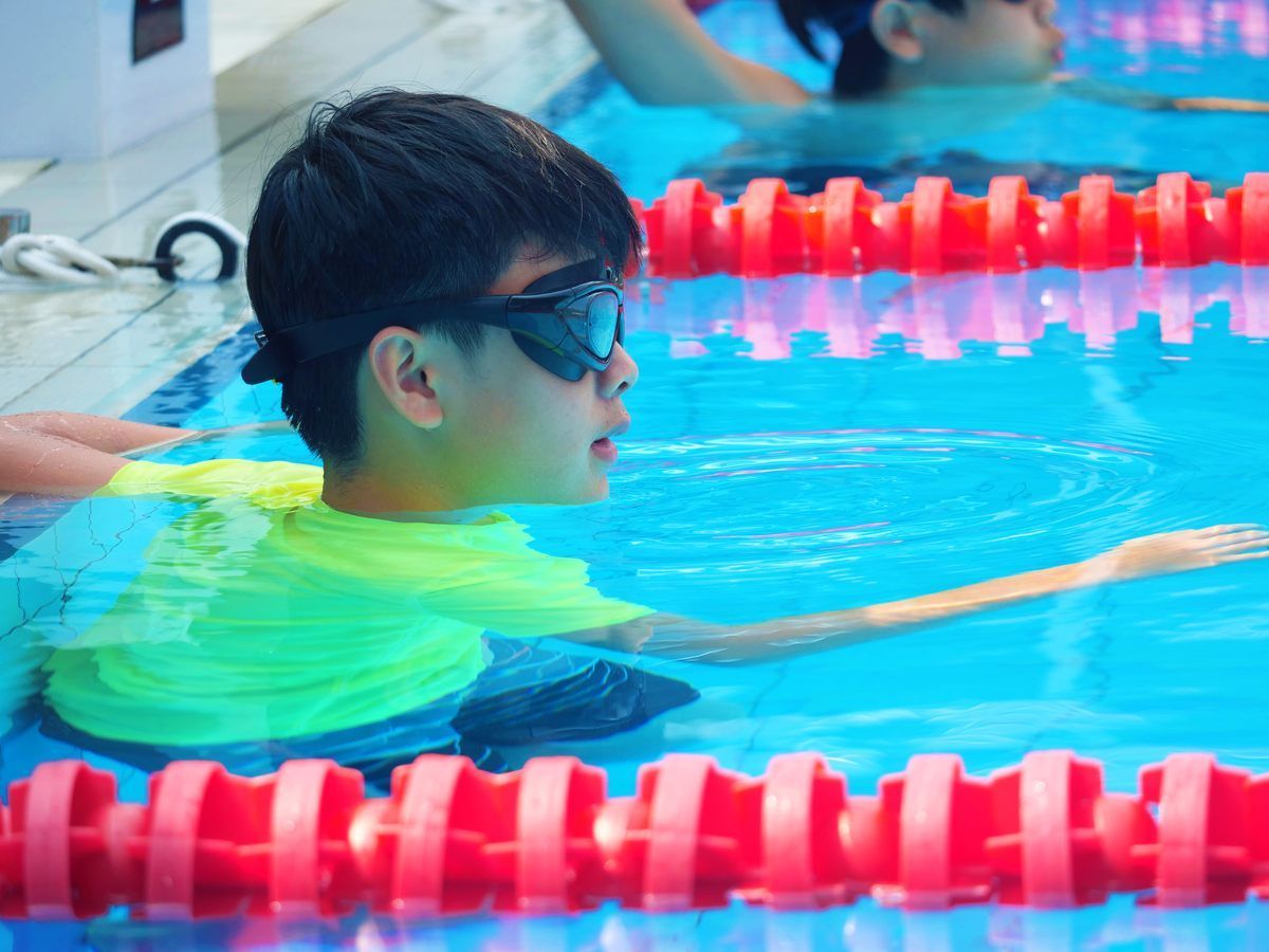 A young boy wearing goggles is swimming in a pool.