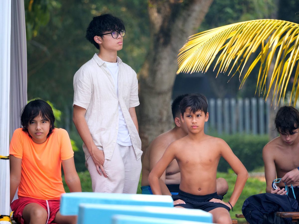 A group of young boys are sitting and standing near a pool.