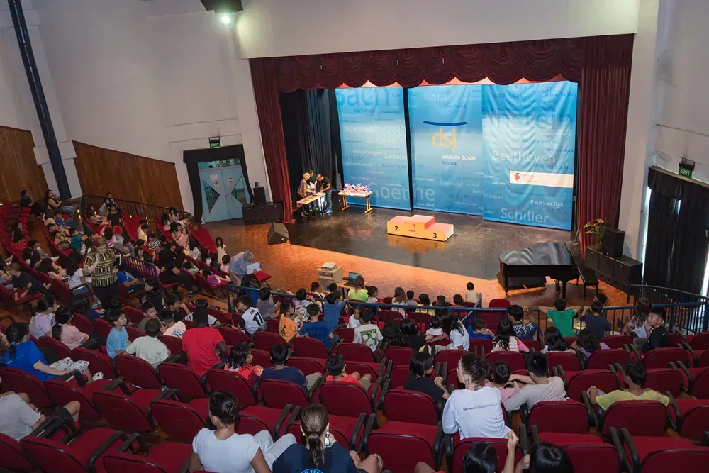 A large group of people are sitting in an auditorium in front of a stage.