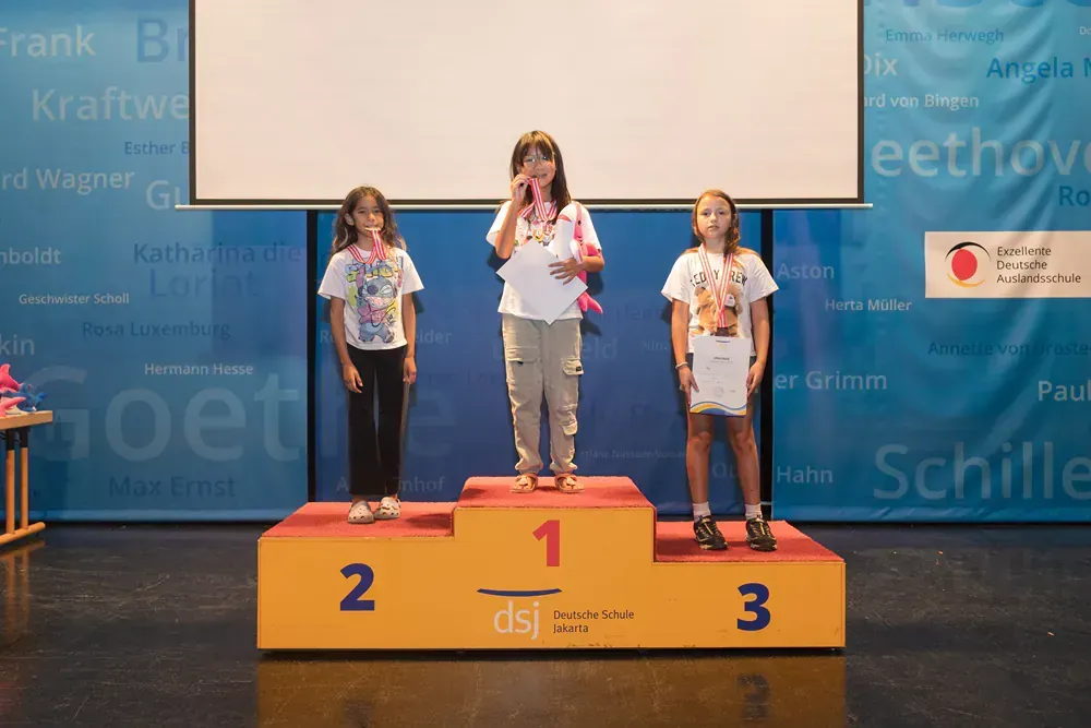 Three girls are standing on a podium with the number 1 2 and 3 on it