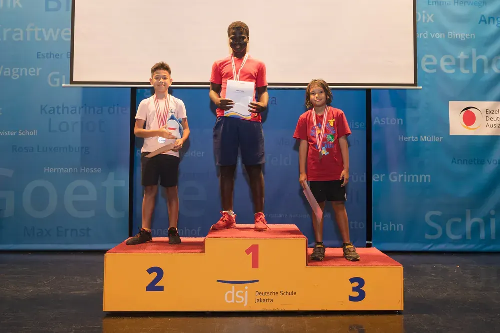 A group of children are standing on a podium holding medals.