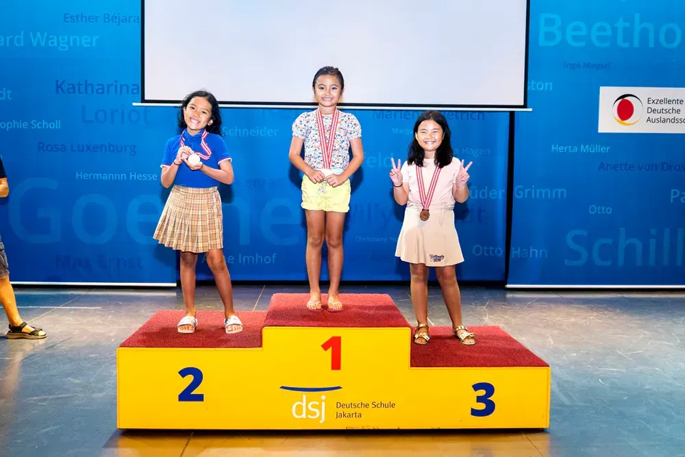 Three young girls are standing on a podium with medals.