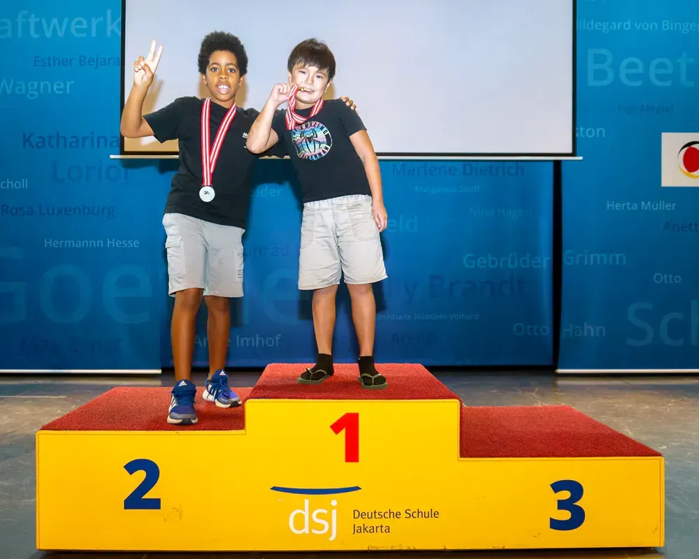 Two boys standing on a podium with the number 1 on it