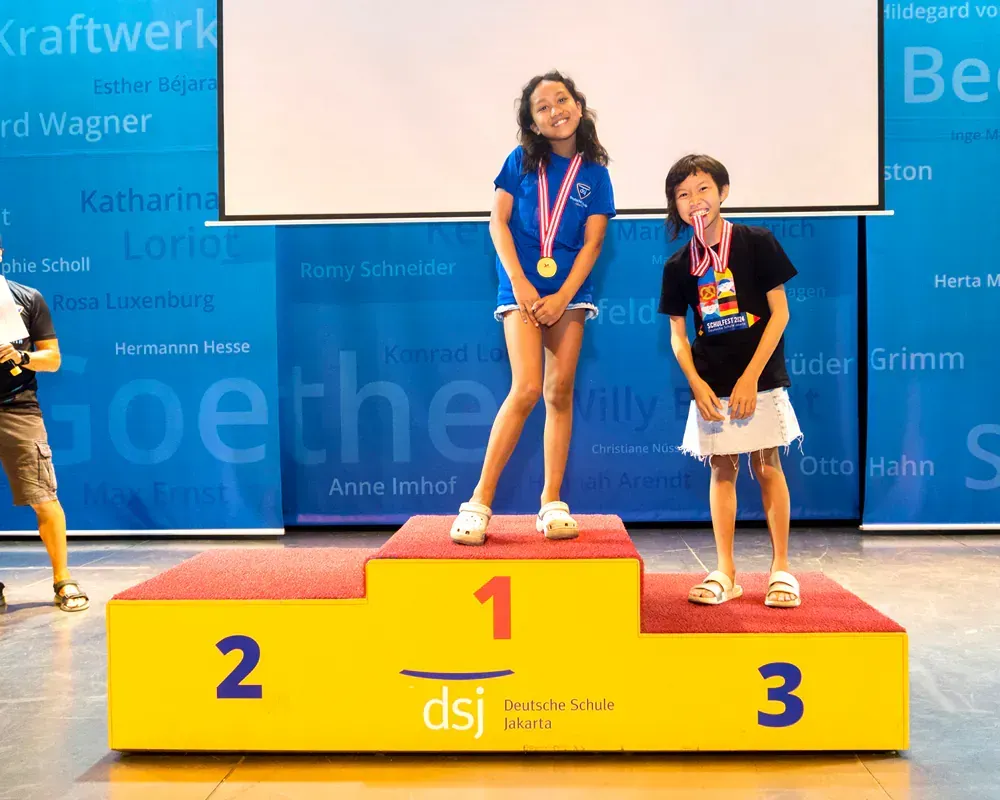Three young girls are standing on a podium with the number 1 on it